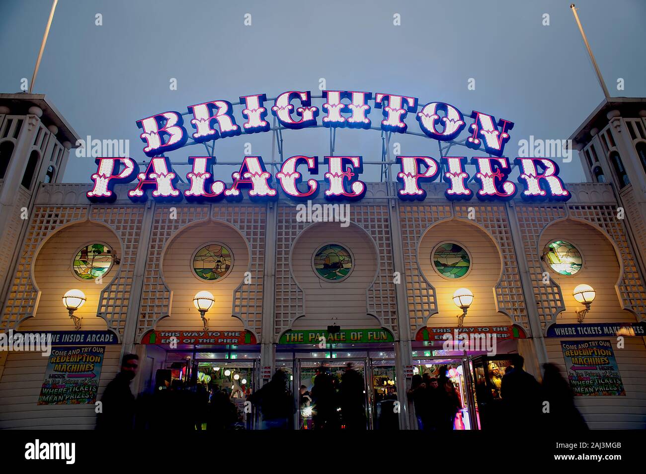 The colourful illuminated sign of Brighton Palace Pier is lit up at dusk. The famous pier in Brighton is one of the U.K.'s most popular tourist sights. Stock Photo