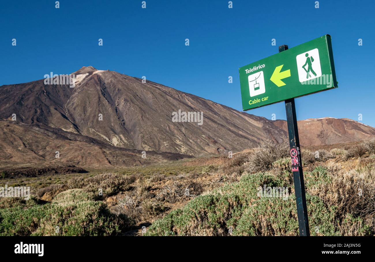 Teide National Park, Tenerife, Spain - December 19, 2019: Green signpost pointing towards the cable car to the summit of Teide, with the mountain itse Stock Photo