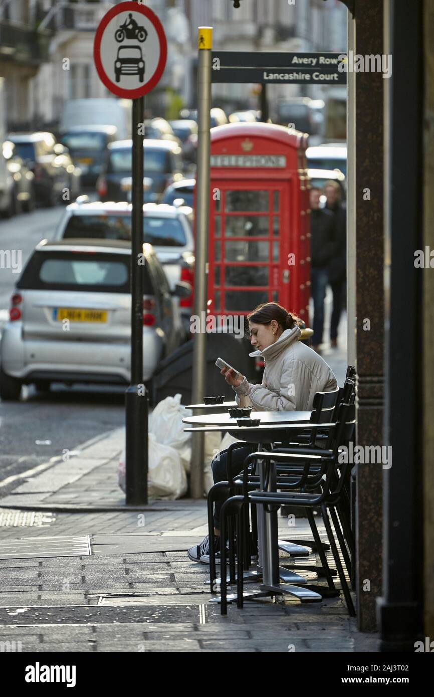 London street scene with lady browsing her phone outside a small restaurant.. Stock Photo