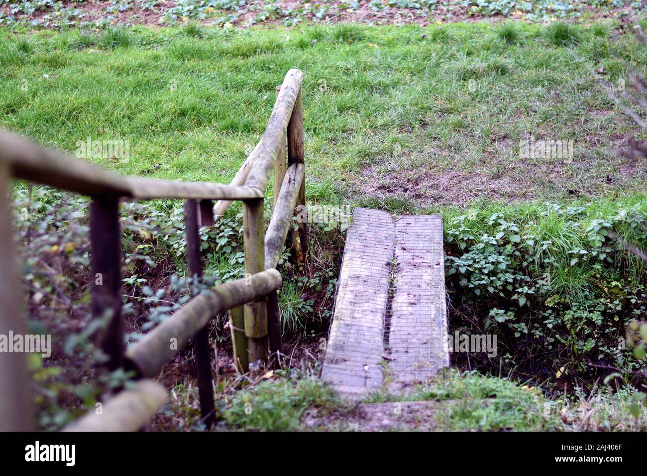 Small wooden foot bridge with railing over ditch in arable field in England Stock Photo