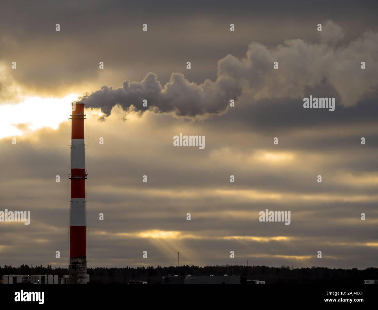 Stock Photo - Big industrial red and white pipe with smoke going outside. Toxic smoke pollutes the atmosphere. Factory pipe polluting air, environmental problems. Dark clouds on the background. Toning Stock Photo