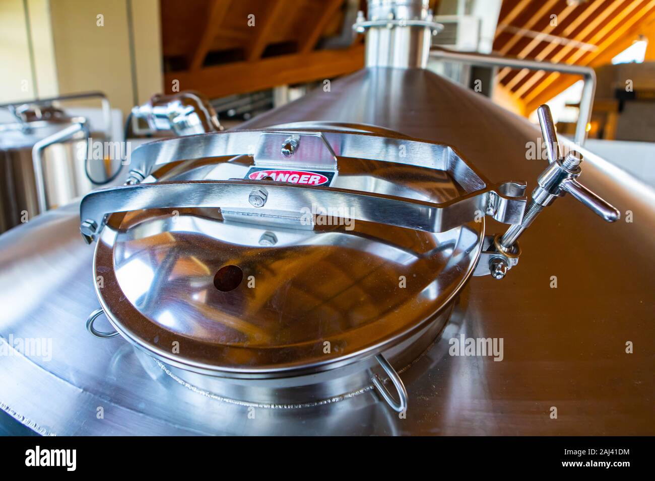 stainless steel tank, vessel closed rounded top manway, manhole door danger sign, brewhouse brewery beer factory machine, selective focus view Stock Photo