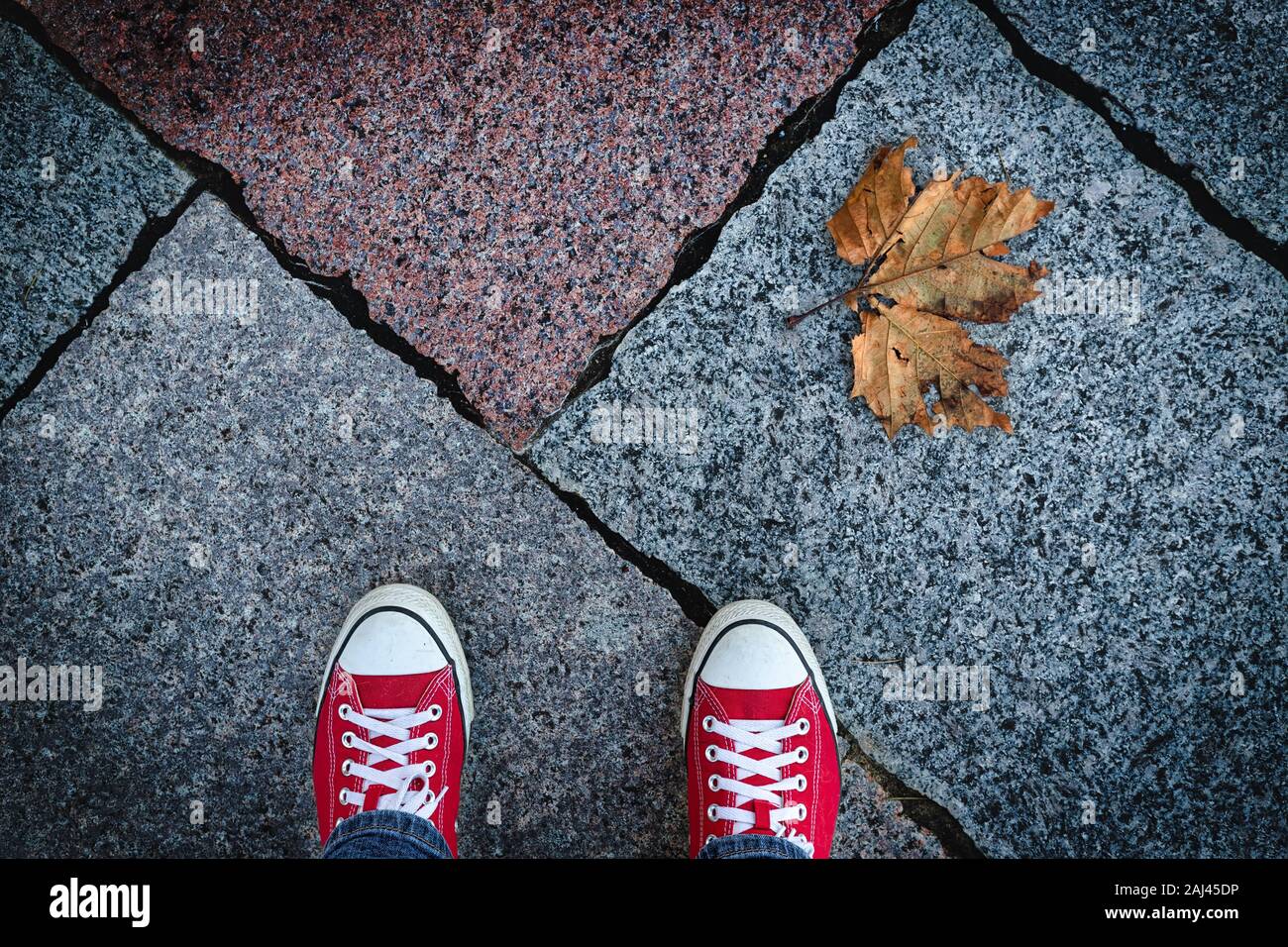 Looking down at my red shoes and a lone leaf on the sidewalk. Stock Photo