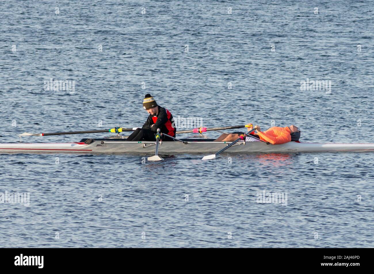 Two young sportsmen one lying tired after practice race in racing rowing boat on Lough Leane