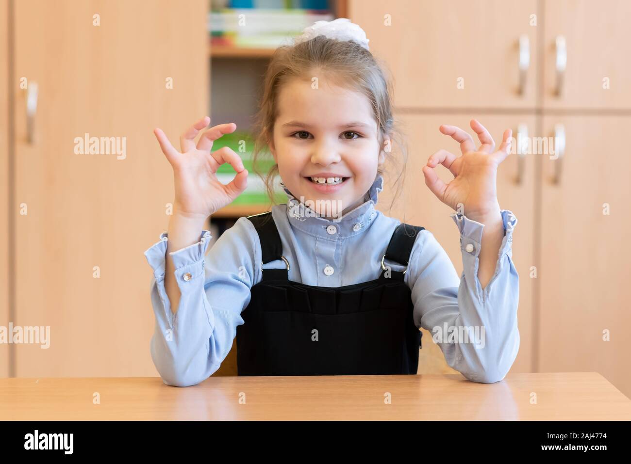 Girl schoolgirl sits at her desk and shows the sign okay Stock Photo ...