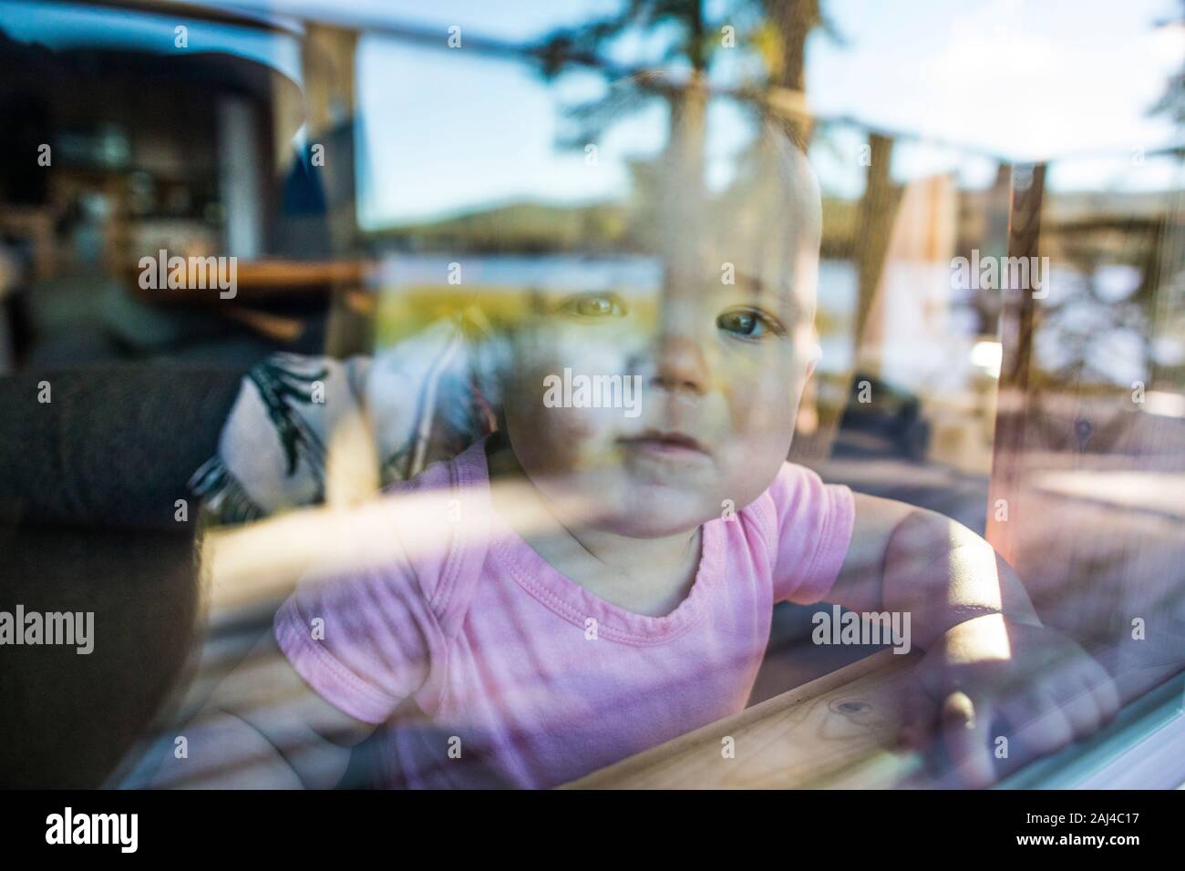 Young toddler girl looks out window with curious expectation. Stock Photo