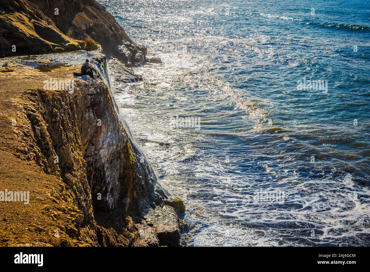 A couple sits at the edge of Alamere Falls on a sunny day in Point Reyes National Seashore, California, USA Stock Photo