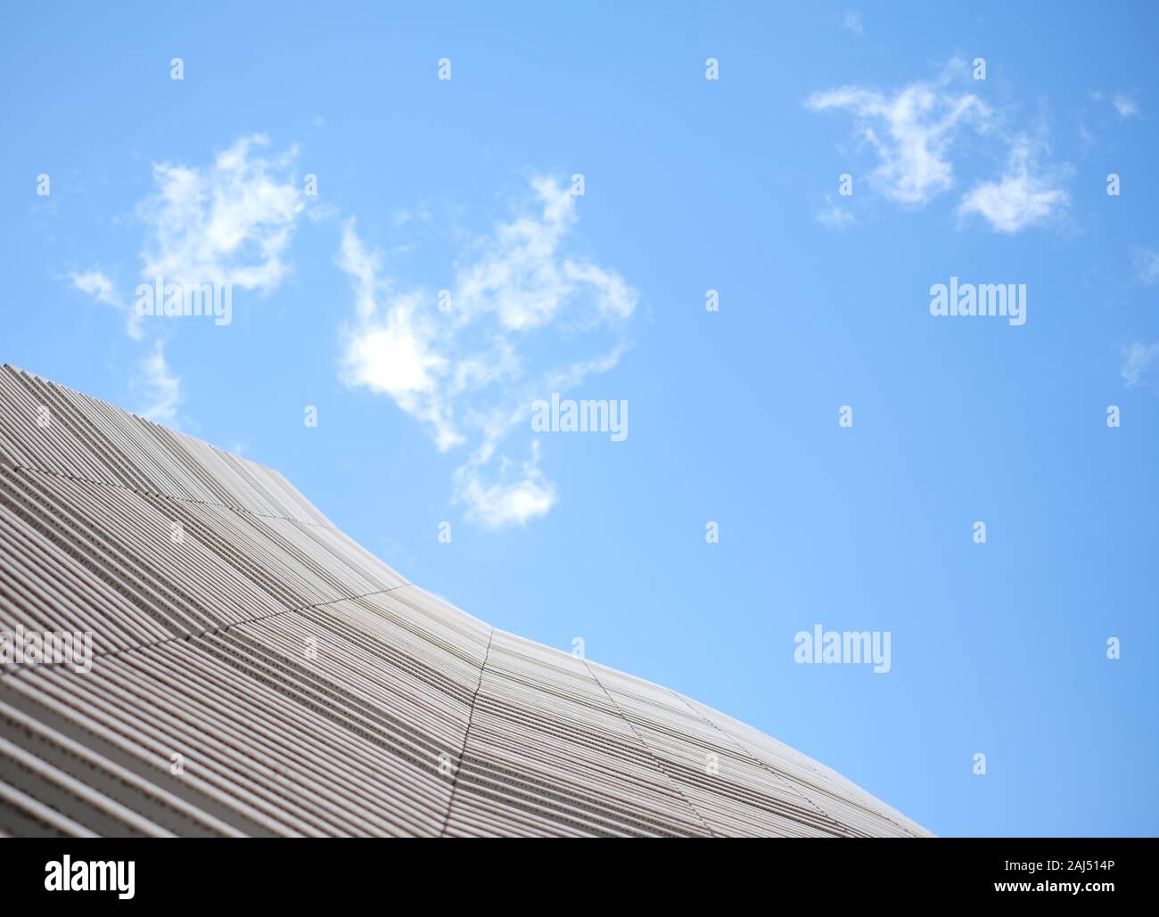 Undulating wavy facade of a clean white modern building, abstract architecture with blue sky and fluffy clouds. Stock Photo