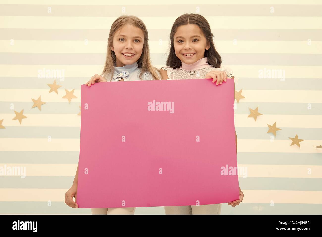 For your text. Happy children holding empty sheet of paper. Little children smiling with pink drawing paper. Small children with blank advertisement p Stock Photo