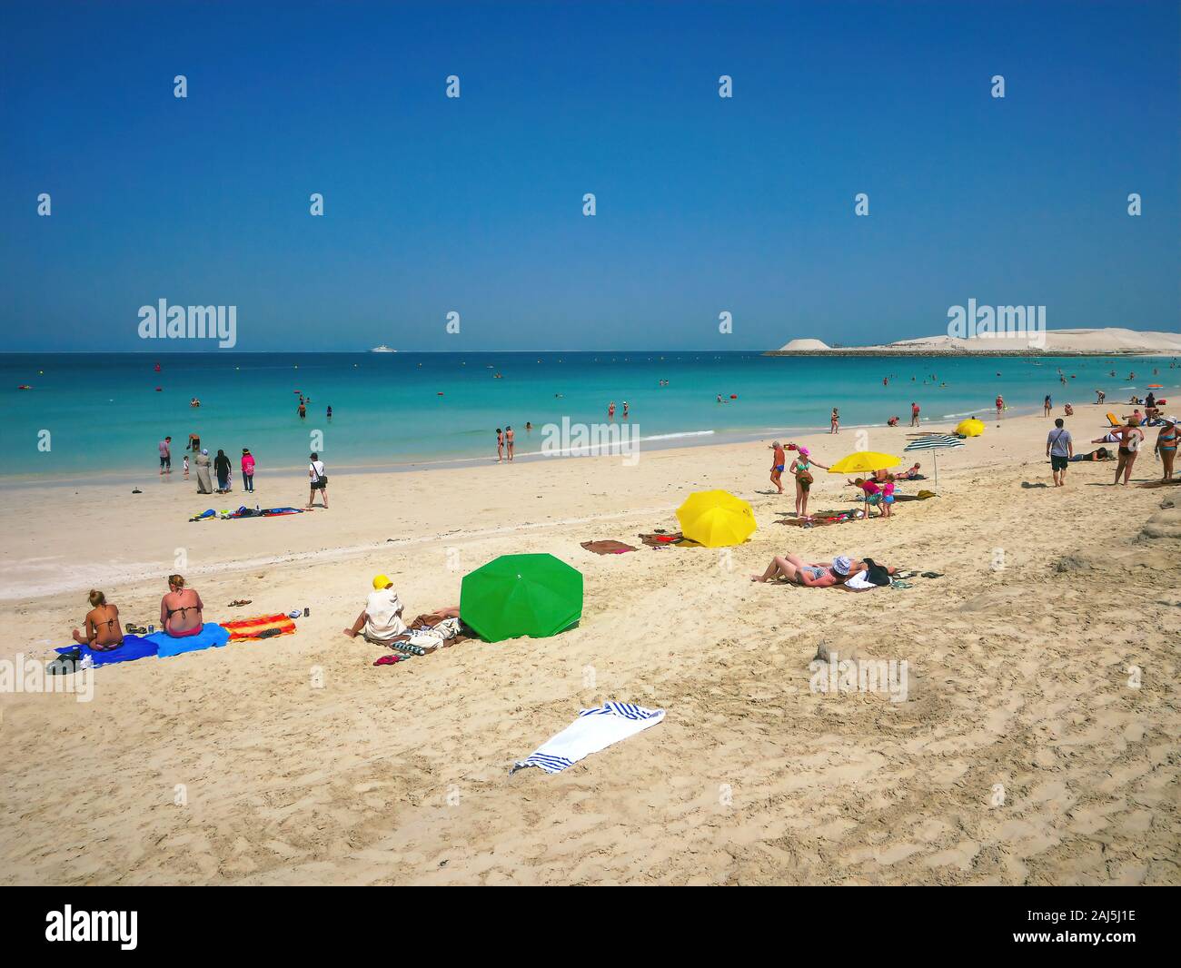 Dubai, UAE - Mar 16, 2013. People sunbathing on Jumeirah Beach in Dubai, and swimming in the turquoise water of the Arabian Gulf on a sunny day. Stock Photo