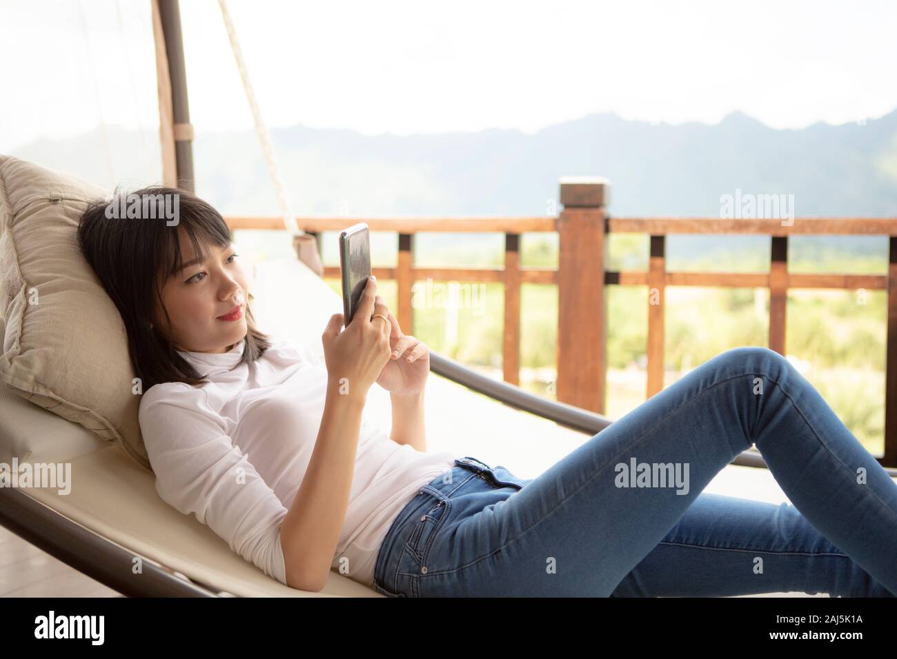 asian younger woman toothy smiling with happiness holding smart phone in hand ,relaxing lifestyle Stock Photo