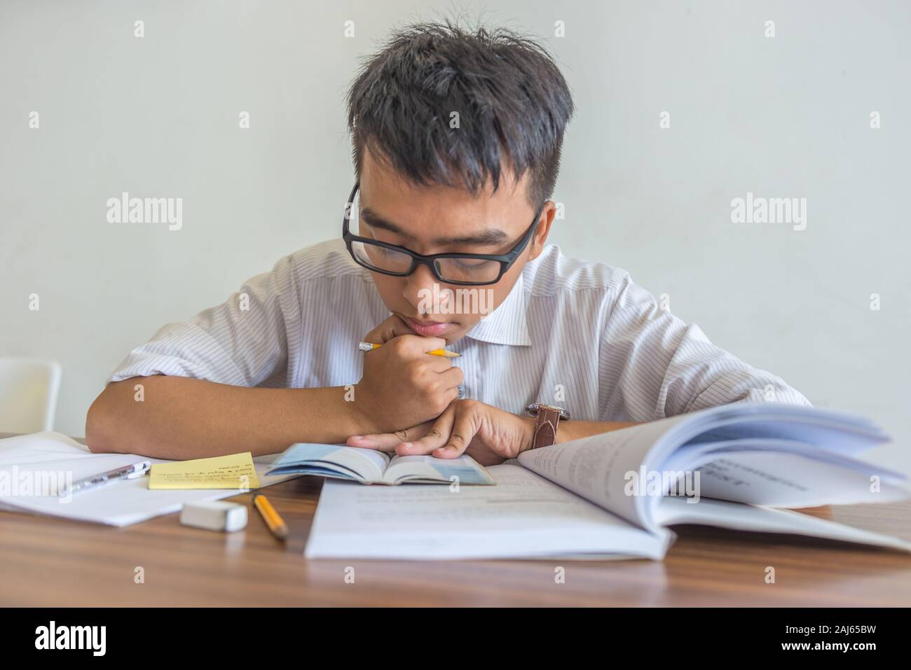 Young Asian student falling asleep while doing homeworks Stock Photo