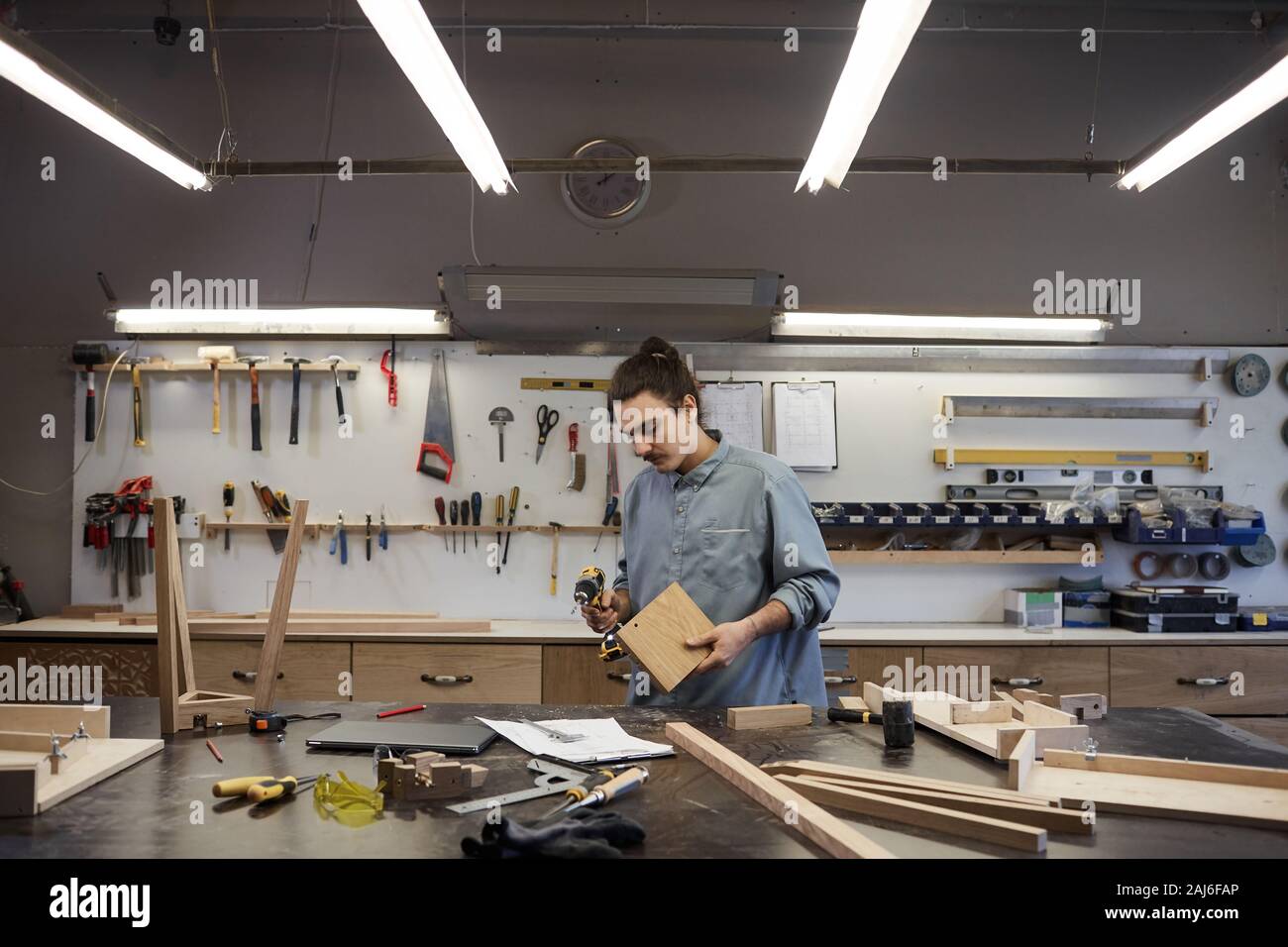 Serious worker making different things from wooden details and using drill in workshop Stock Photo