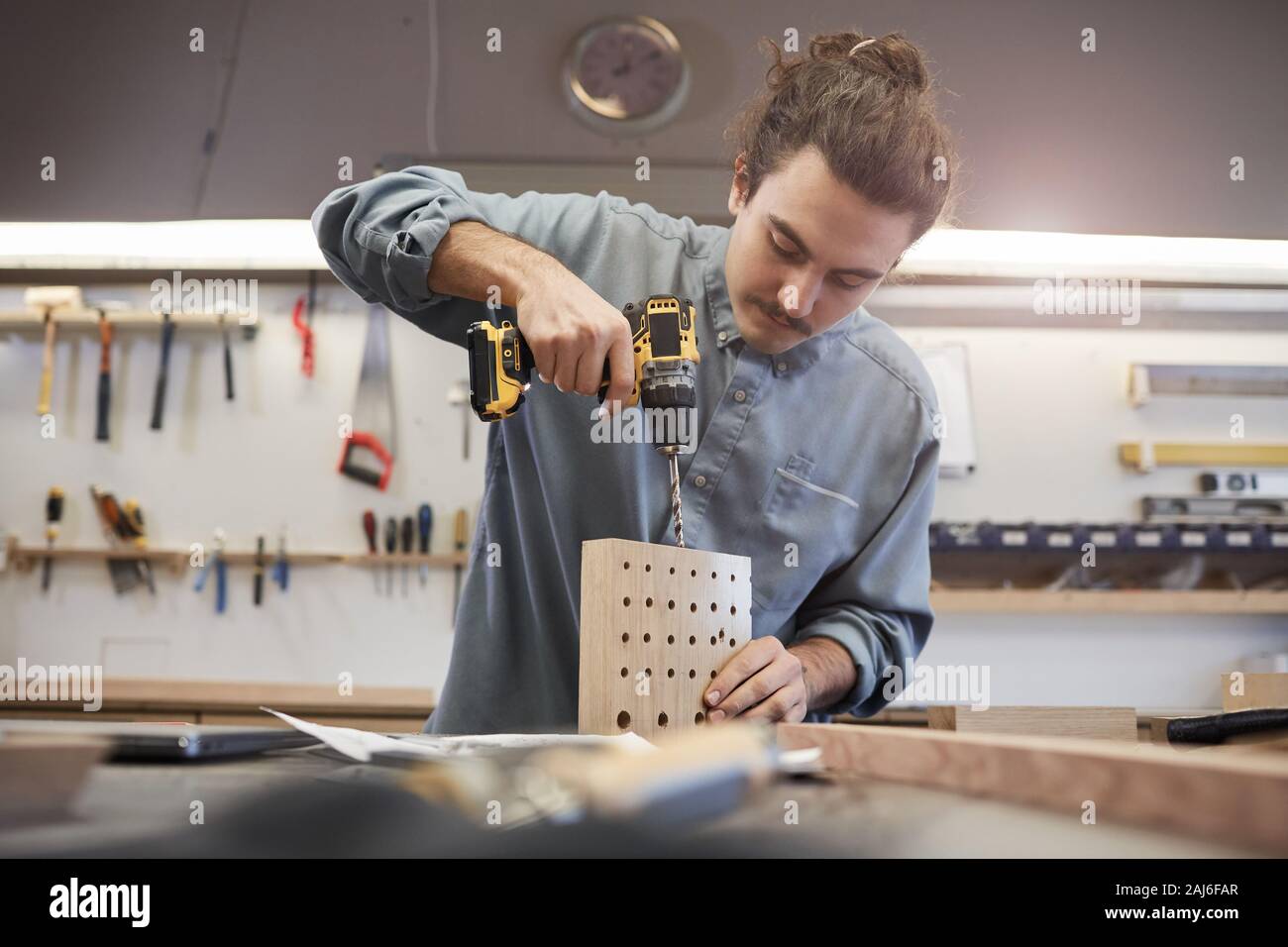 Young man making holes with drill in wooden details while working in workshop Stock Photo