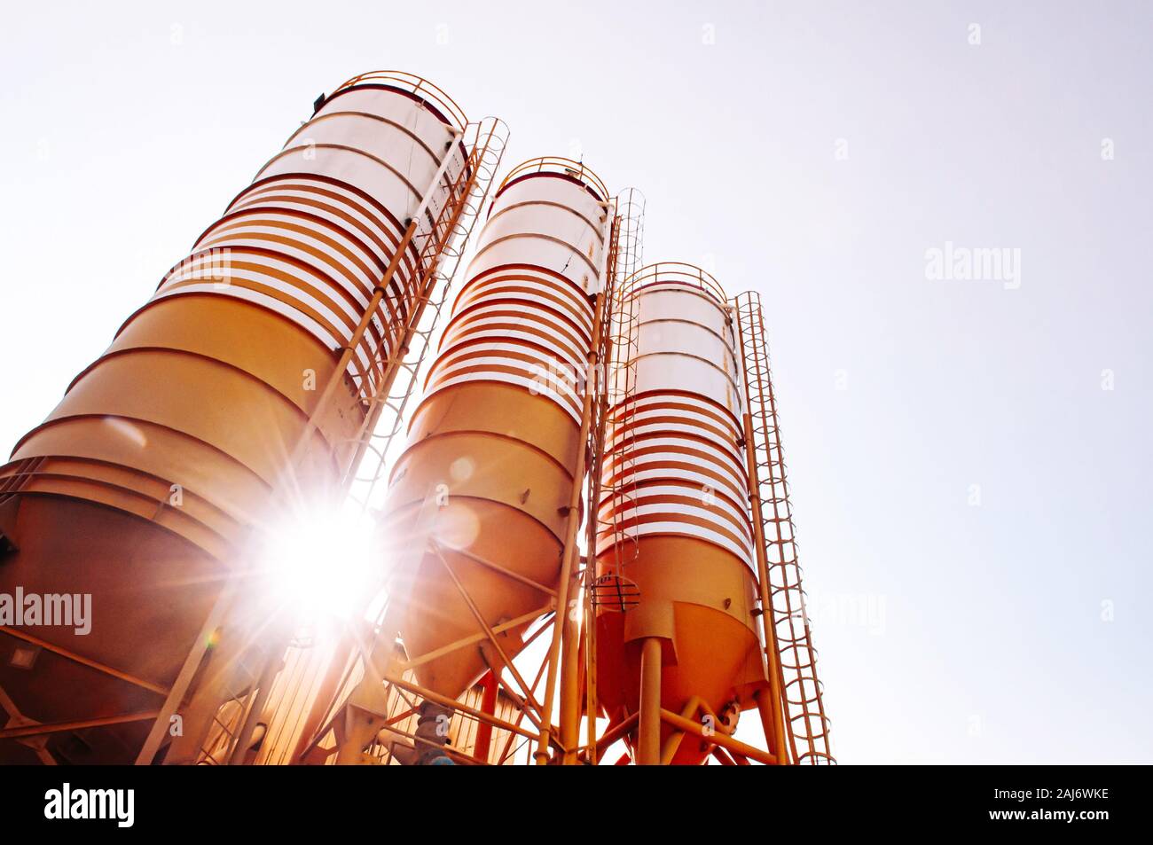 Cement silos of Cement batching plant factory against evening sun flare with warm clear sky Stock Photo