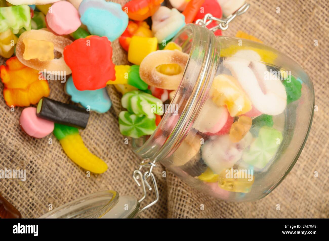 Multicolored shaped marmalade in a glass jar on a background of rough homespun fabric close-up. Delicious holiday treat Stock Photo