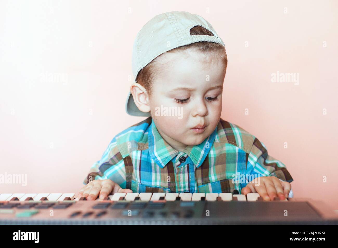 Portrait of a pretty boy wearing baseball cap backwards playing the digital piano. Training of the child in music. Stock Photo