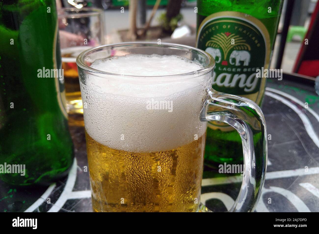 Glass with foamy Chang beer, bottle on background. Chang (Elephant in English) is ThaiBev's flagship brand. Stock Photo