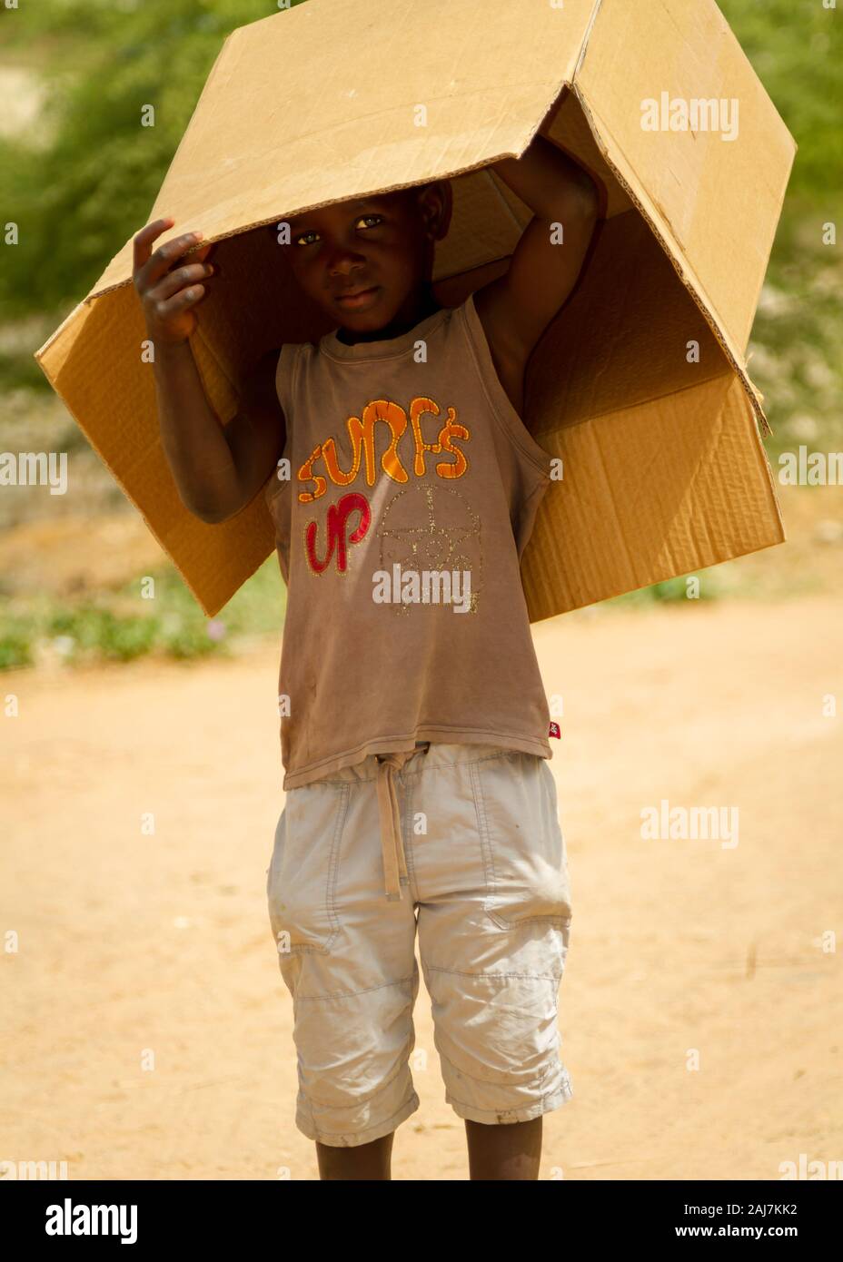 Young Senegalese boy peeking out from under an old cardboard box outside on a dusty road in Saly, Senegal, Africa - Photograph: Tony Taylor Stock Photo