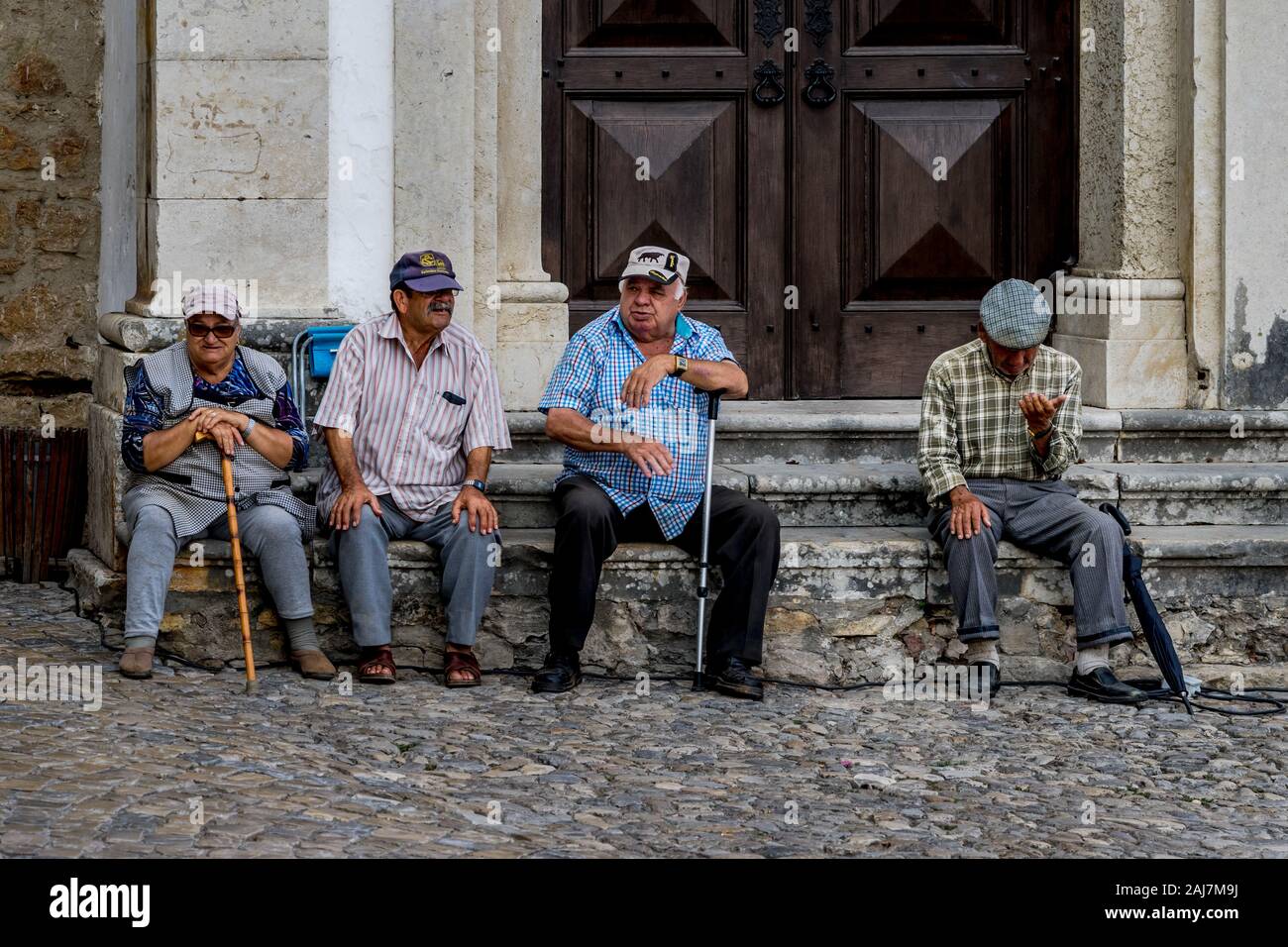 Elderly men hanging out as friends sitting on the steps infant of the entrance of an old building in Obidos, Portugal. Photograph: Iris de Reus Stock Photo