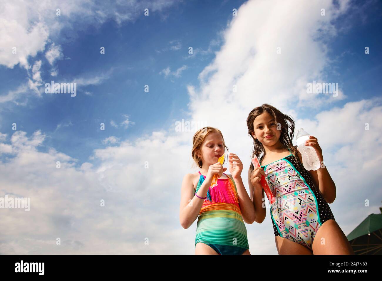 Two Young Girls in Swimsuits With Frozen Treats Against Blue Sky Stock Photo