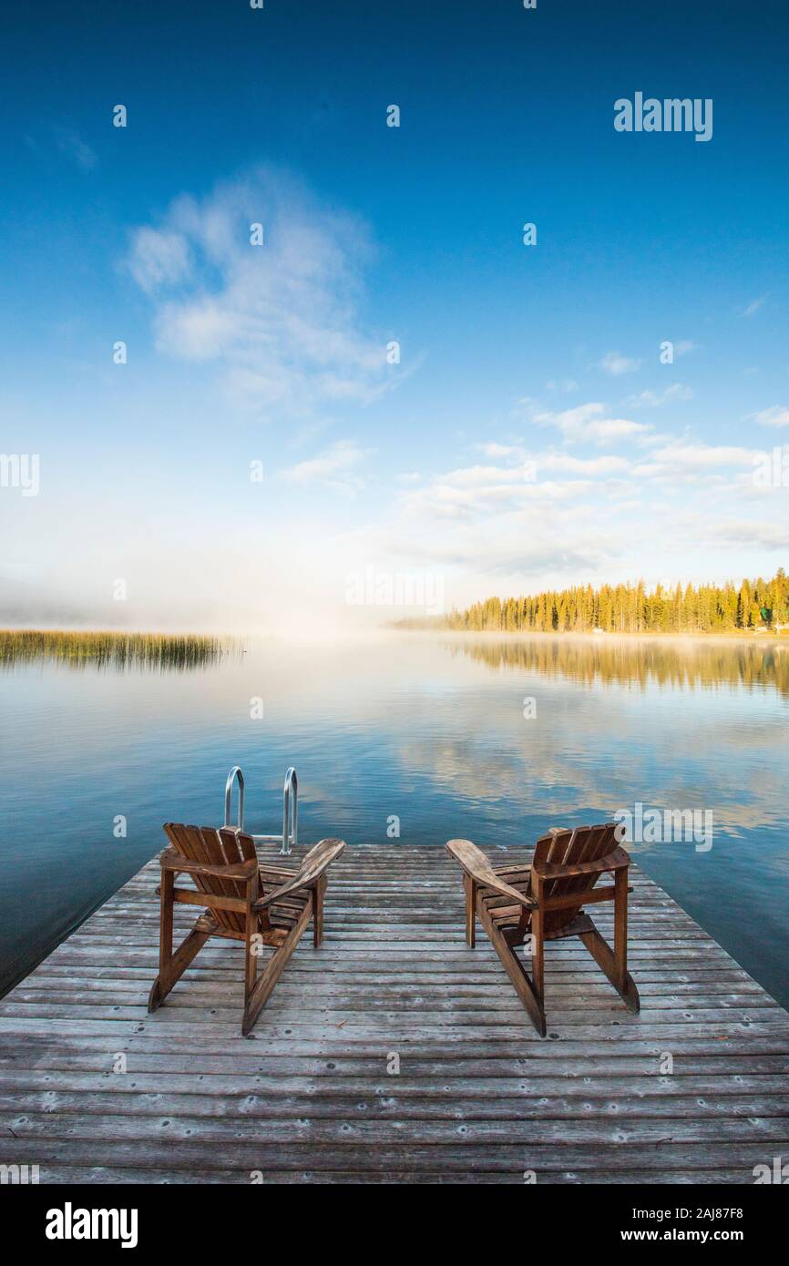 Wooden chairs on dock looking over lake at dawn Stock Photo - Alamy