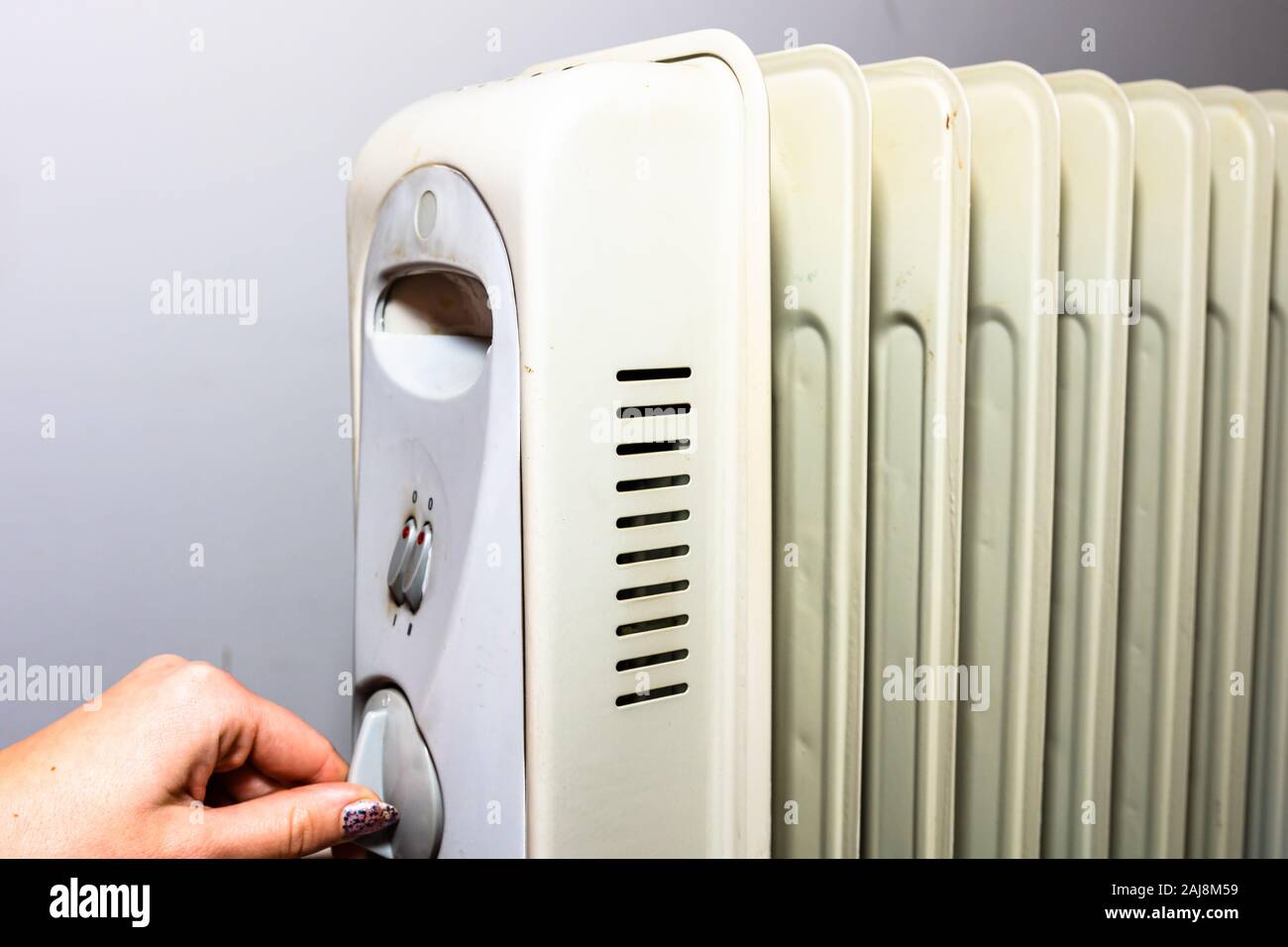 Hands turning on the oil radiator heater on white background Stock