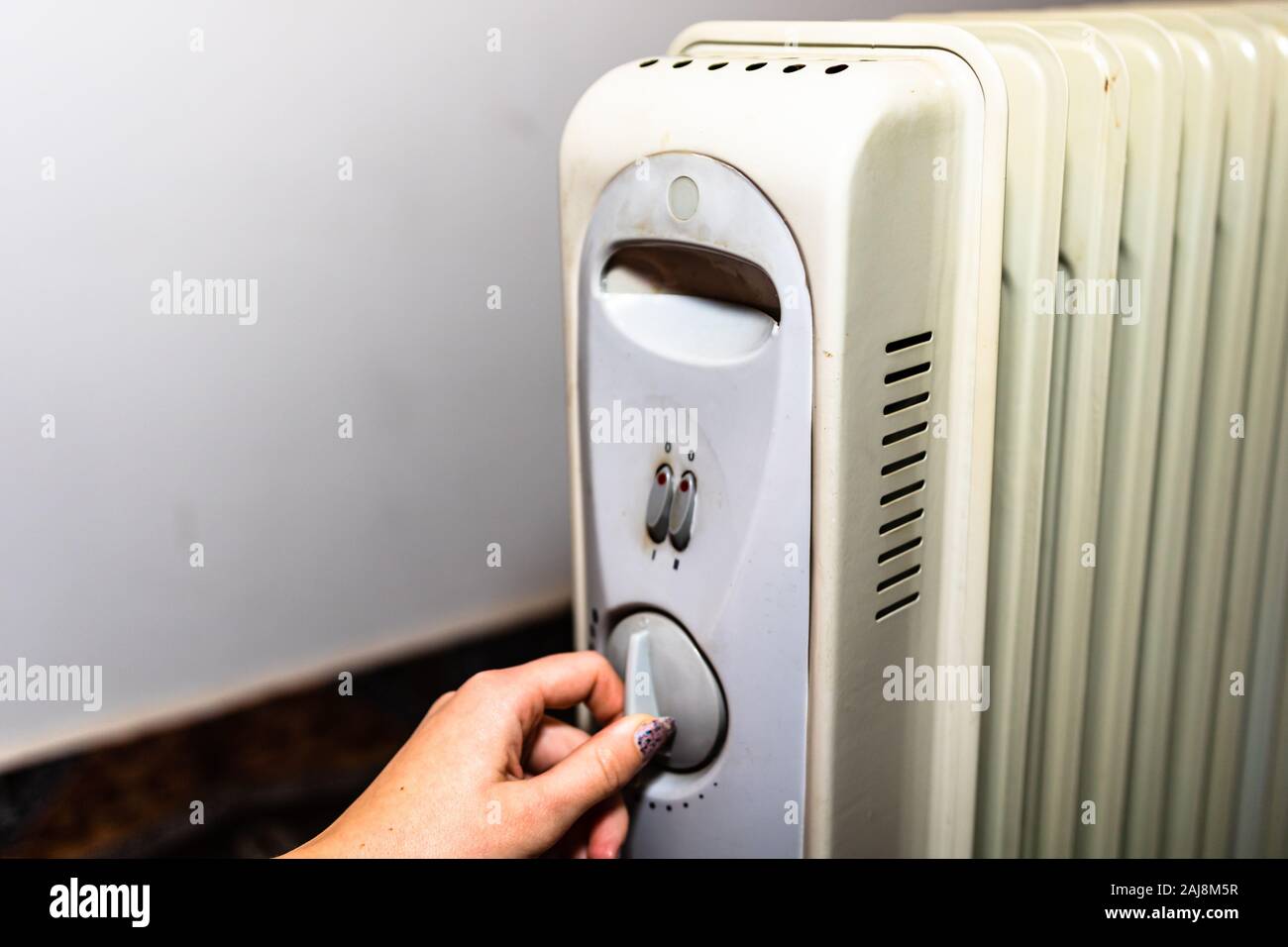Hands turning on the oil radiator heater on white background Stock