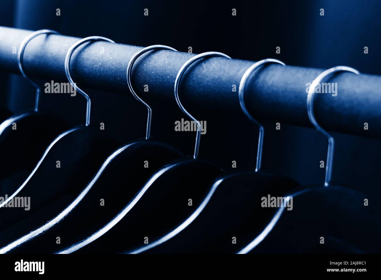 Contrasting empty hangers hang on a floor hanger. Tinted in color classic blue. Color of the year 2020. Stock Photo