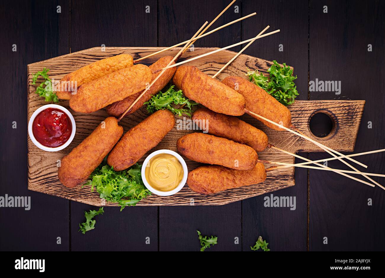 Traditional American corn dogs with mustard and ketchup on wooden board ...