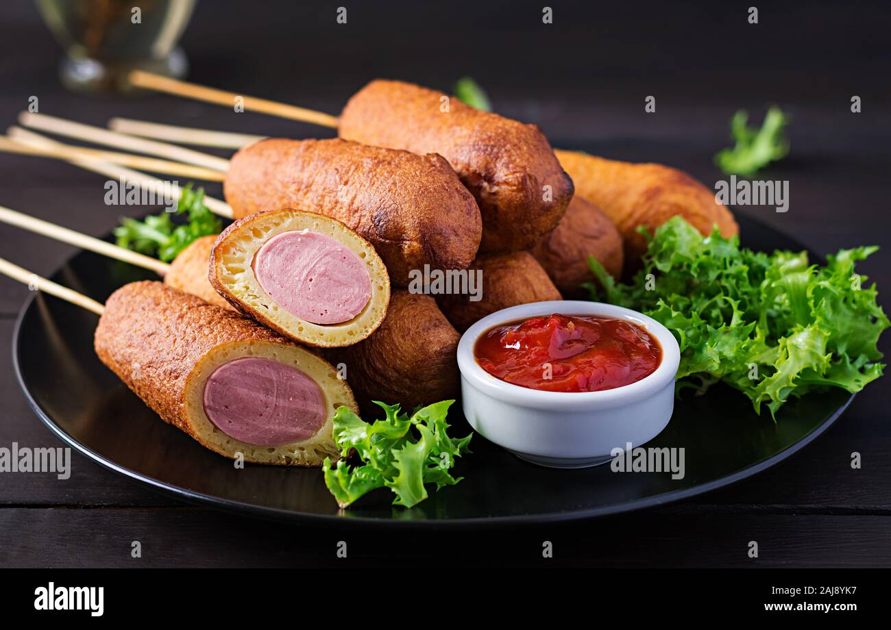 Traditional American corn dogs with mustard and ketchup on black plate. Street food. Copy space Stock Photo