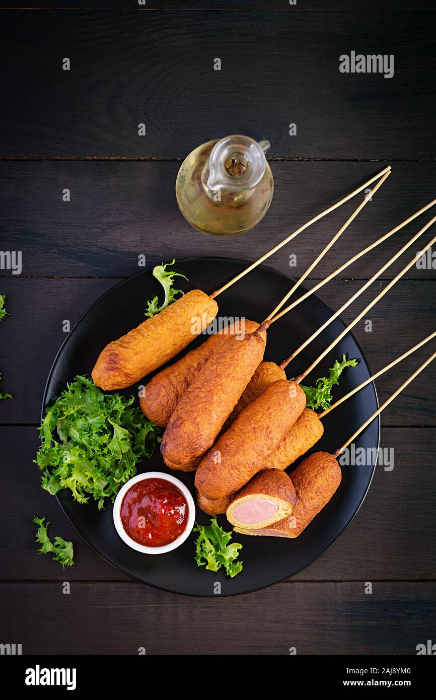Traditional American corn dogs with mustard and ketchup on black plate. Street food. Top view, copy space Stock Photo
