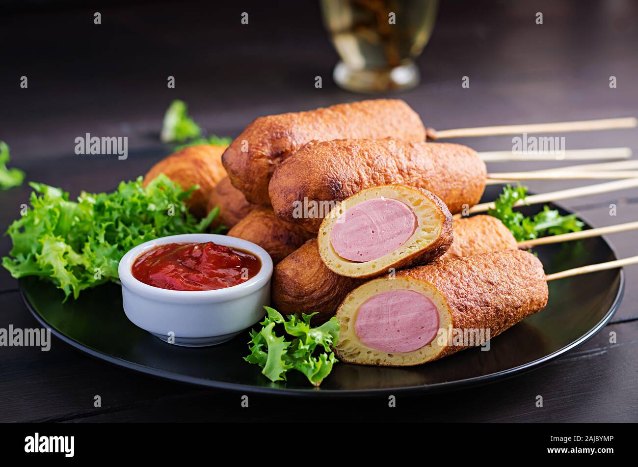 Traditional American corn dogs with mustard and ketchup on black plate. Street food. Copy space Stock Photo