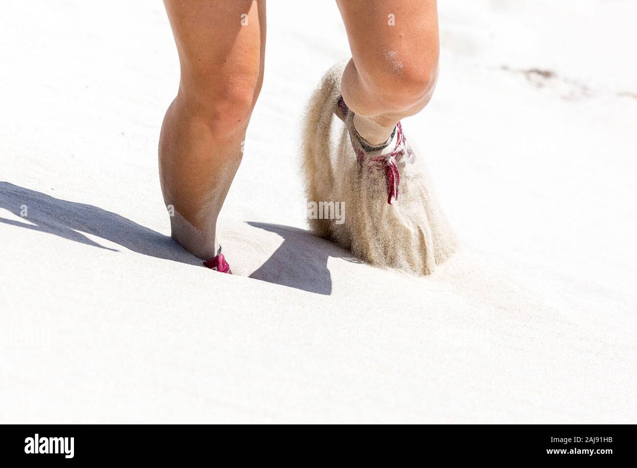 Close up of the legs of a woman wearing pink shoes walking on a white sand dune, De Hoop Nature Reserve, South Africa Stock Photo