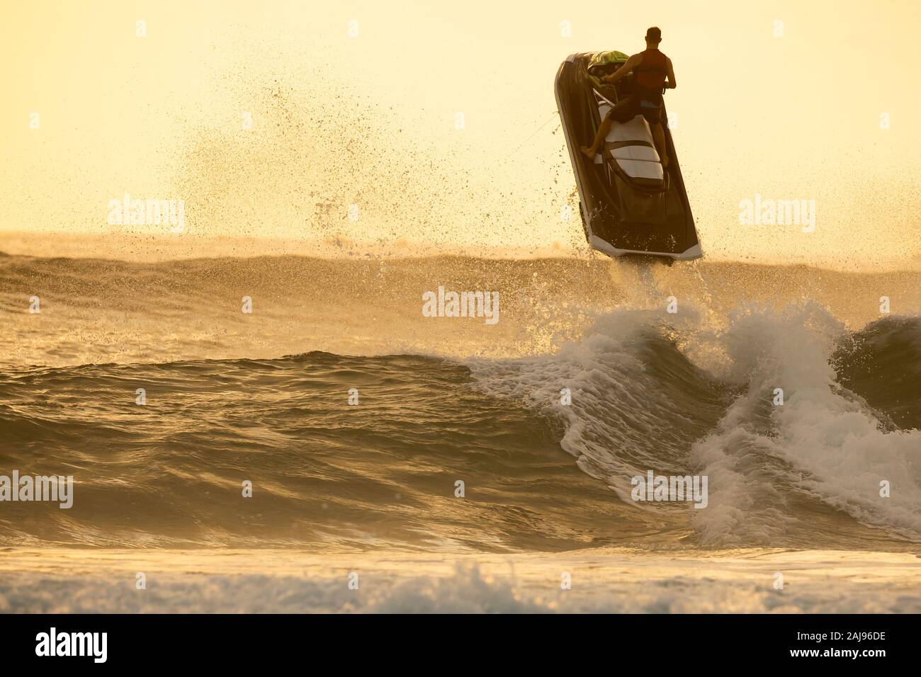 Silhouette of man riding a water scooter and jumping over a wave on sunrise Stock Photo