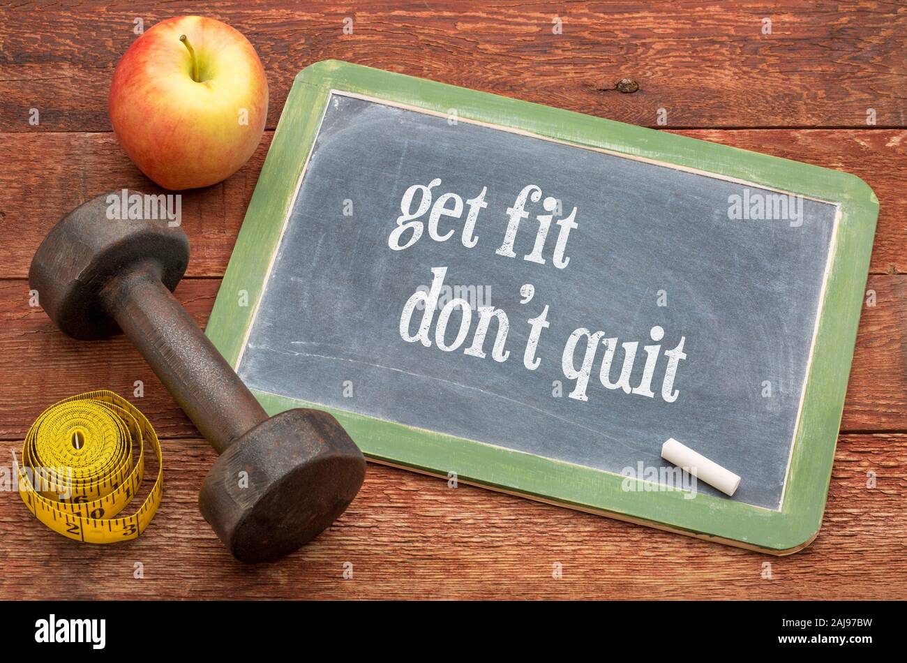 Get fit, do not quit. -  slate blackboard sign against weathered red painted barn wood with a dumbbell, apple and tape measure, Fitness and determinat Stock Photo