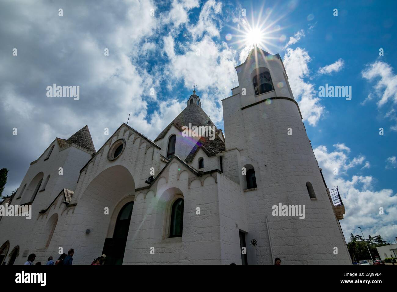 ALBEROBELLO, ITALY - AUGUST 28, 2018 - Town of Alberobello with whitewashed Trulli cone stone tile roof houses in Apulia is visited each year by millions of tourists. Church with sun light diffraction Stock Photo