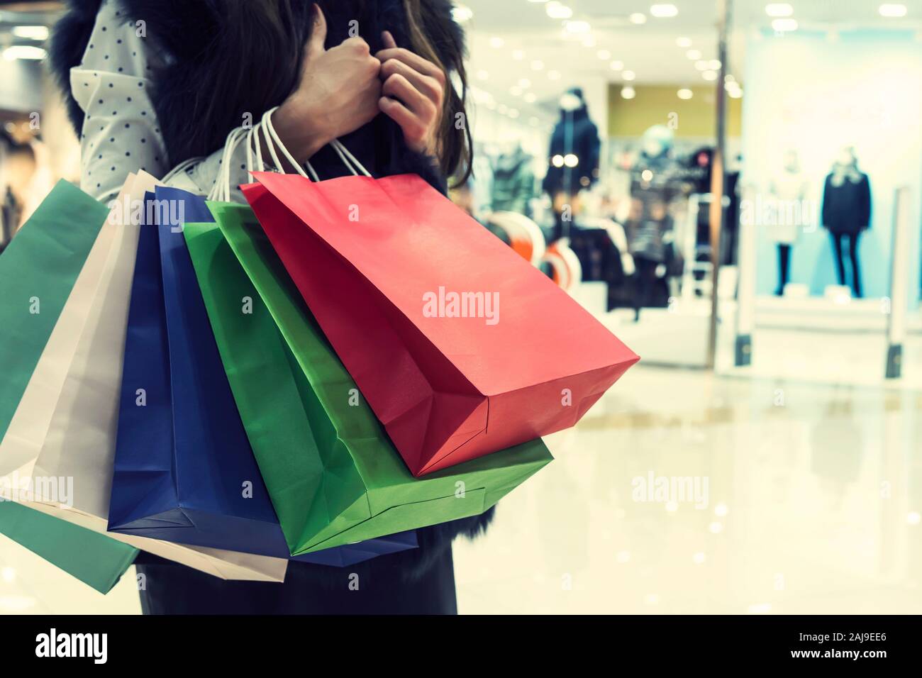 Crop unrecognizable girl clasping many shopping bags on mall background. Lady making many purchases in store. Concept of female incidentals. Looking f Stock Photo