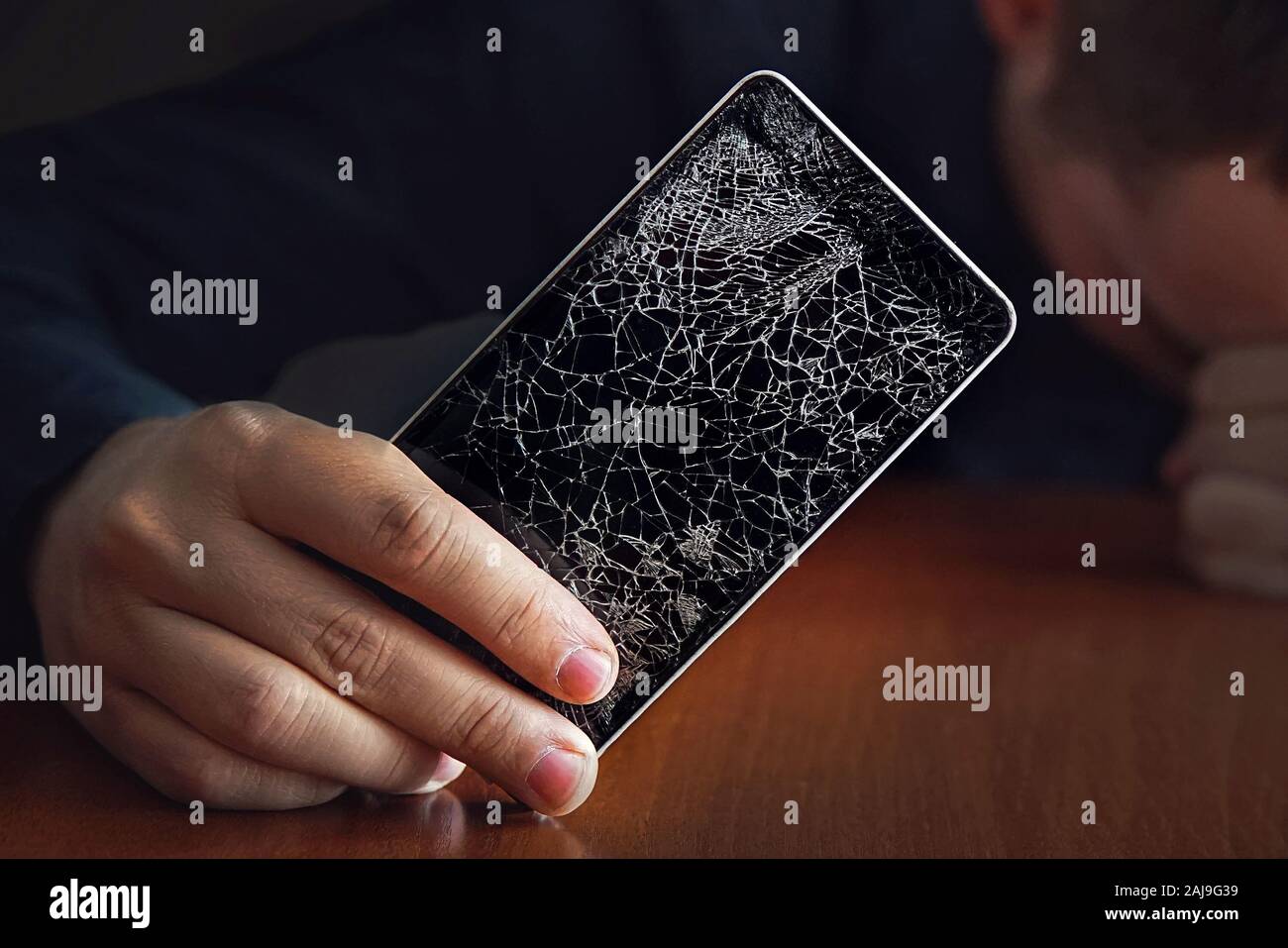 Handsome angry businessman showing broken smartphone with crashed screen. a large crack in the form of a web on the smartphone screen close-up. Stock Photo