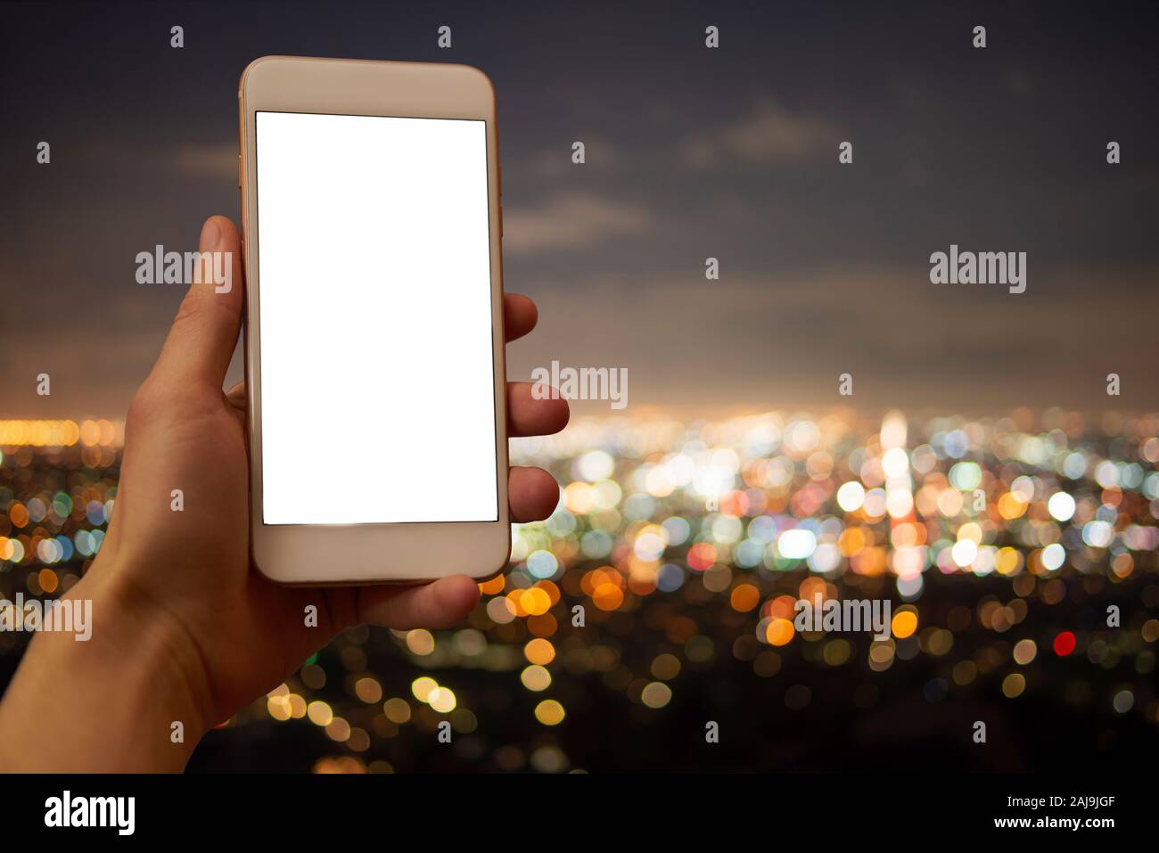 Hand holding a mobile phone with blank display, unsharp city lights in the background Stock Photo