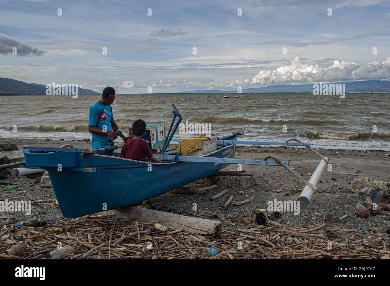 Palu City, Central Sulawesi, Indonesia. 3rd Jan, 2020. A fisherman accompanied by his son repairing a broken boat engine.High waves in the waters of Palu Bay forced Hundreds of fishermen in the village of Lere to anchor their boats. According to the Palu Meteorology, Climatology and Geophysics Agency (BMKG) the waves reached two meters to three meters, considered quite dangerous for fishermen. Credit: Opan Bustan/SOPA Images/ZUMA Wire/Alamy Live News Stock Photo