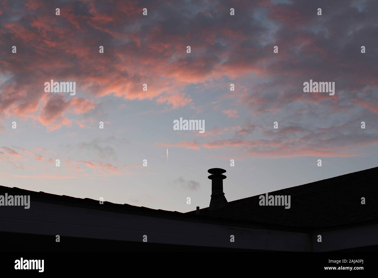 an image of pink clouds, while a skywriting plane is coming towards it. Stock Photo