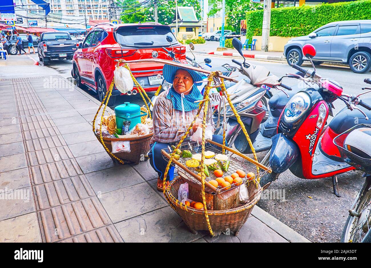 PATONG, THAILAND - APRIL 30, 2019: The street food seller, sitting by the road with her baskets with hot foods (boiled eggs, banana wraps, rice cakes) Stock Photo