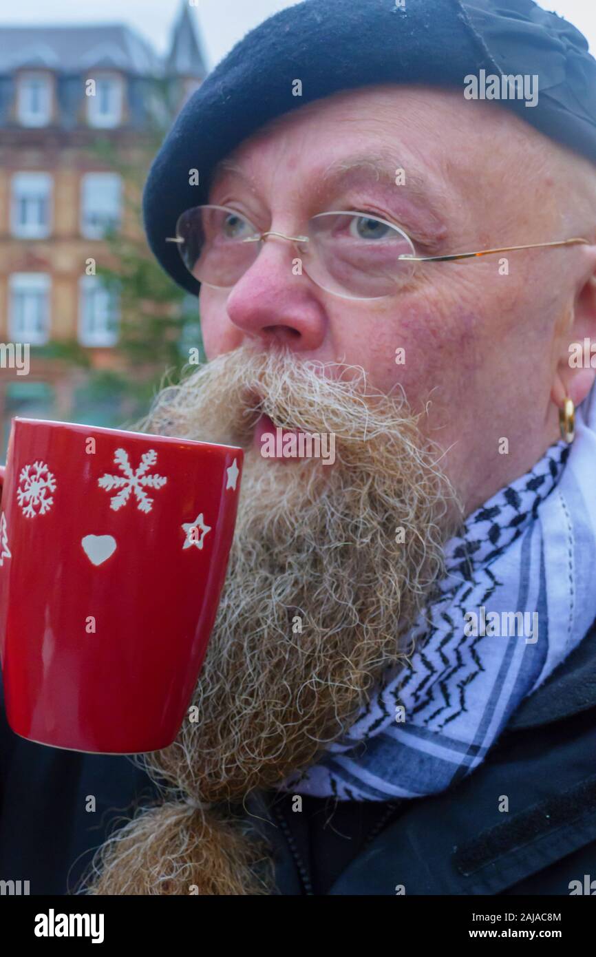 Mann mit langem Bart und Brille, trinkt eine Tasse Glühwein Stock Photo