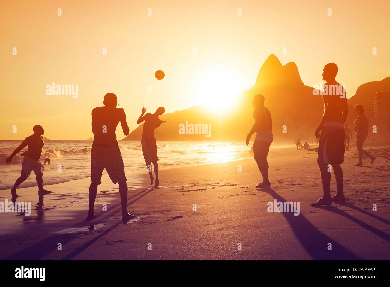 Silhouette of unidentified, unrecognizable locals playing ball at sunset in Ipanema beach, Rio de Janeiro, Brazil. Stock Photo