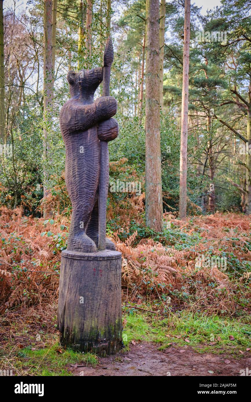Carved wooden sculpture carving of a bear stood to attention with a spear by trail in woodland at Sandringham in Norfolk Stock Photo