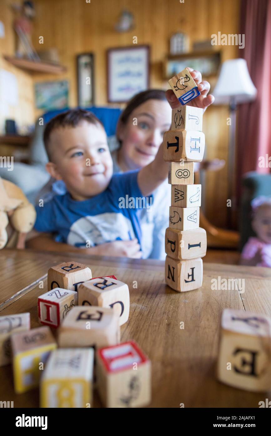 Mother worries as son places wooden block on tower. Stock Photo