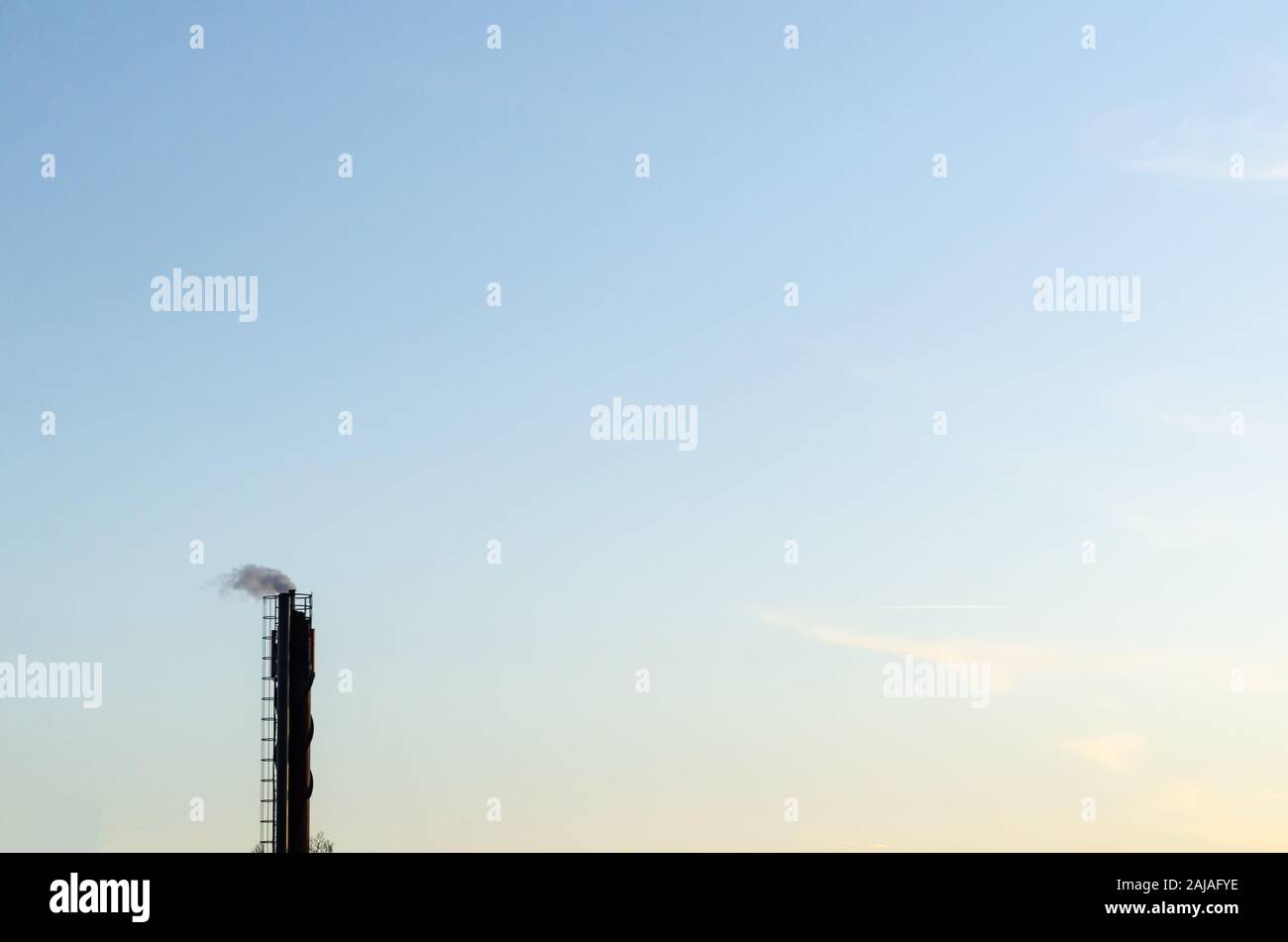 Industrial chimney with smoke by a blue sky Stock Photo