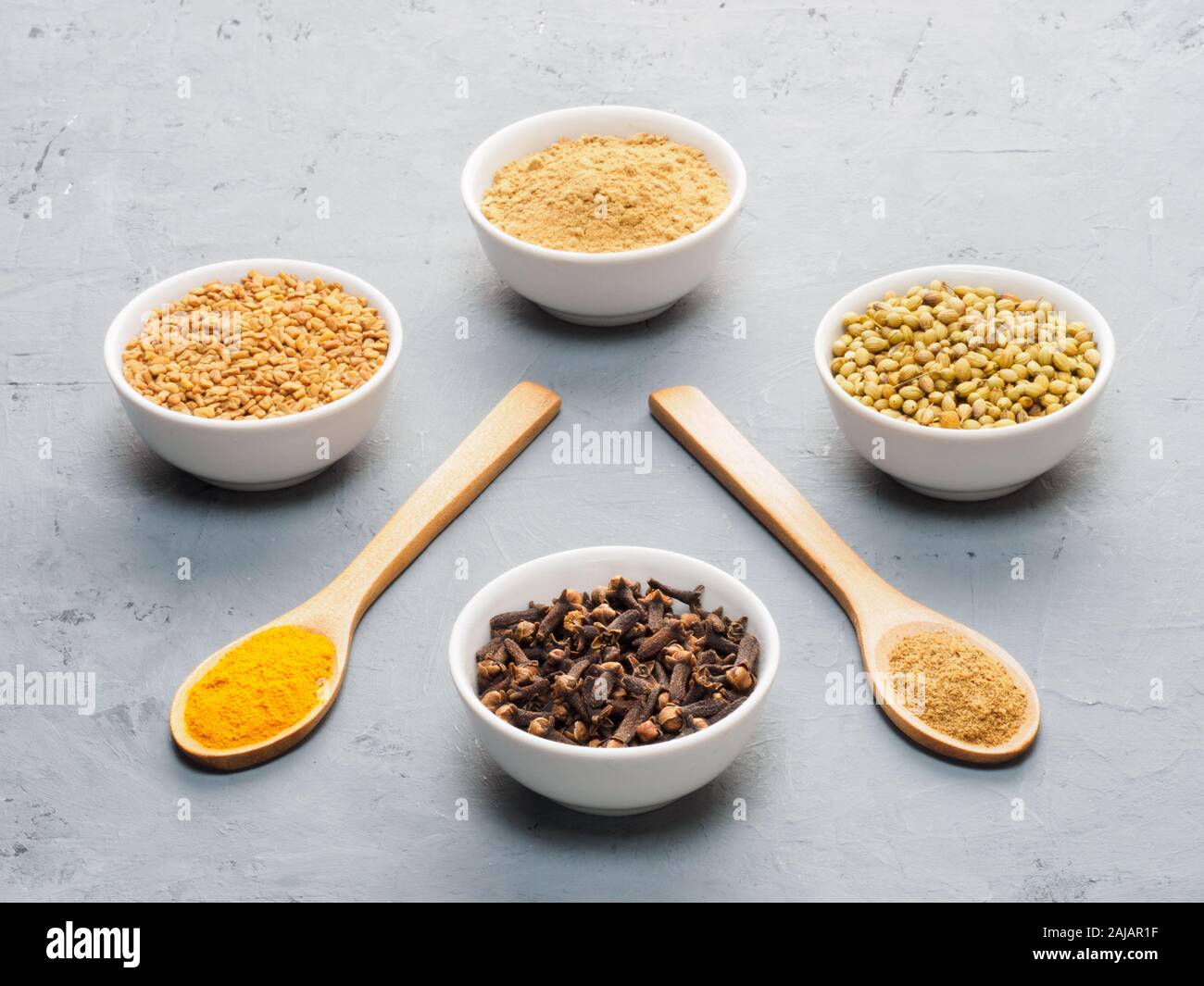 Spice dry ginger, black pepper, masala, turmeric, cloves, coriander in white bowls and spoons on gray concrete background Stock Photo