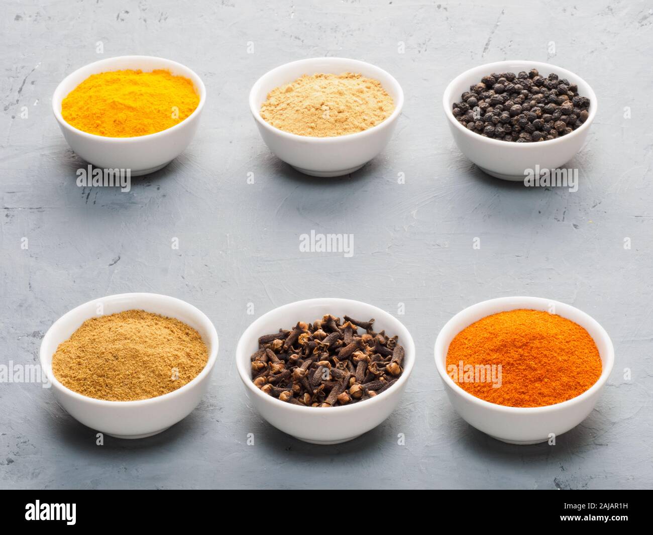 Spice dry ginger, black pepper, masala, turmeric, cloves, red chili in white bowls on gray concrete background Stock Photo